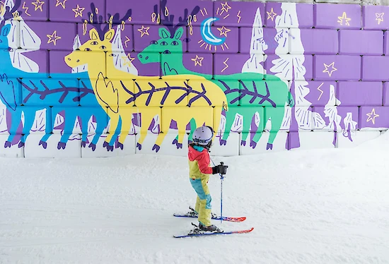 Child skiing with parent on a sunny slope at Revelstoke Mountain Resort during the Kids Ski Free event