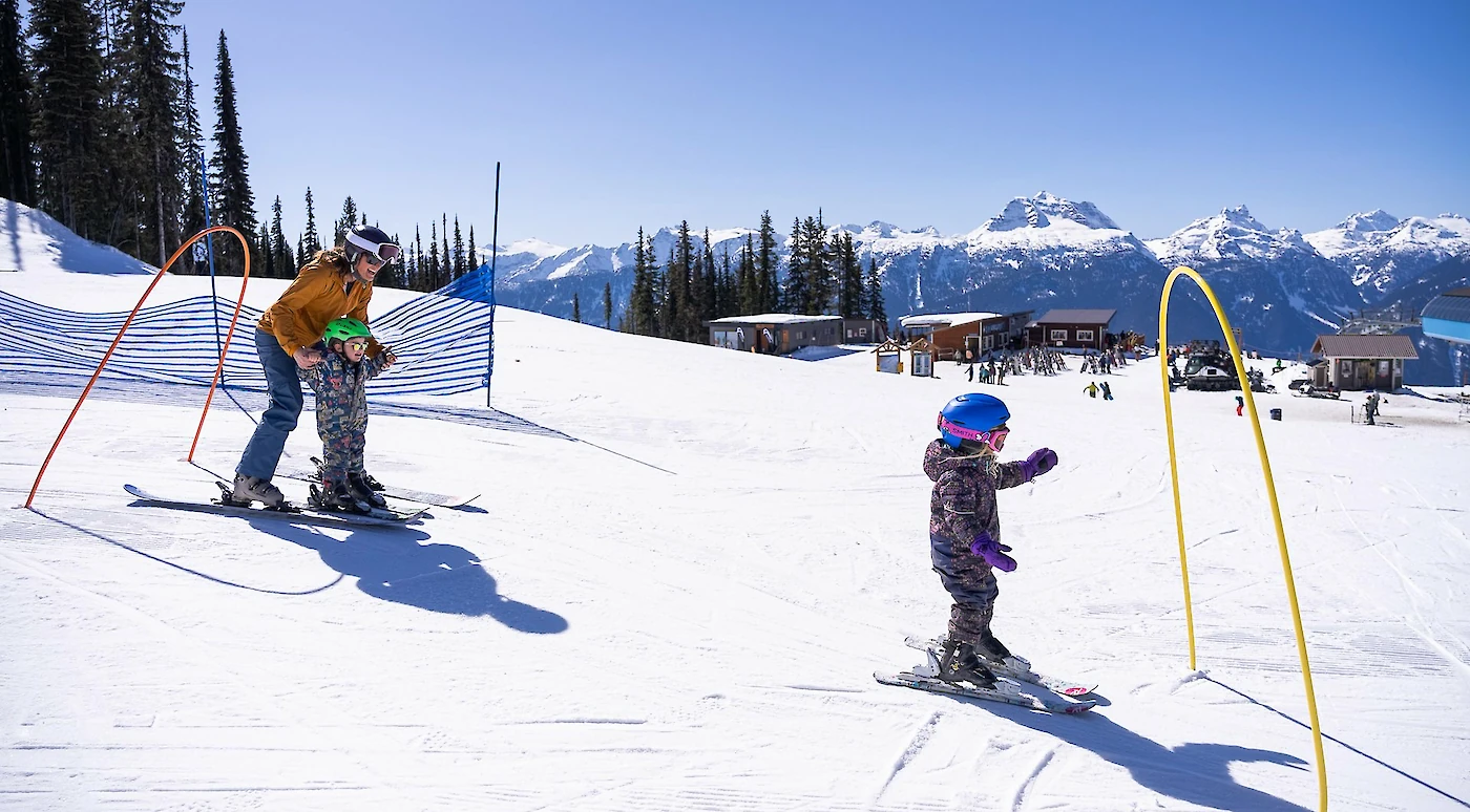 Child skiing with parent on a sunny slope at Revelstoke Mountain Resort during the Kids Ski Free event