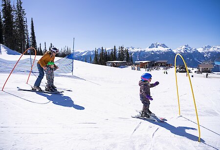 Child skiing with parent on a sunny slope at Revelstoke Mountain Resort during the Kids Ski Free event