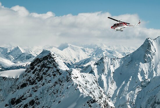 Helicopter soaring above majestic snow-covered mountain peaks under a clear blue sky