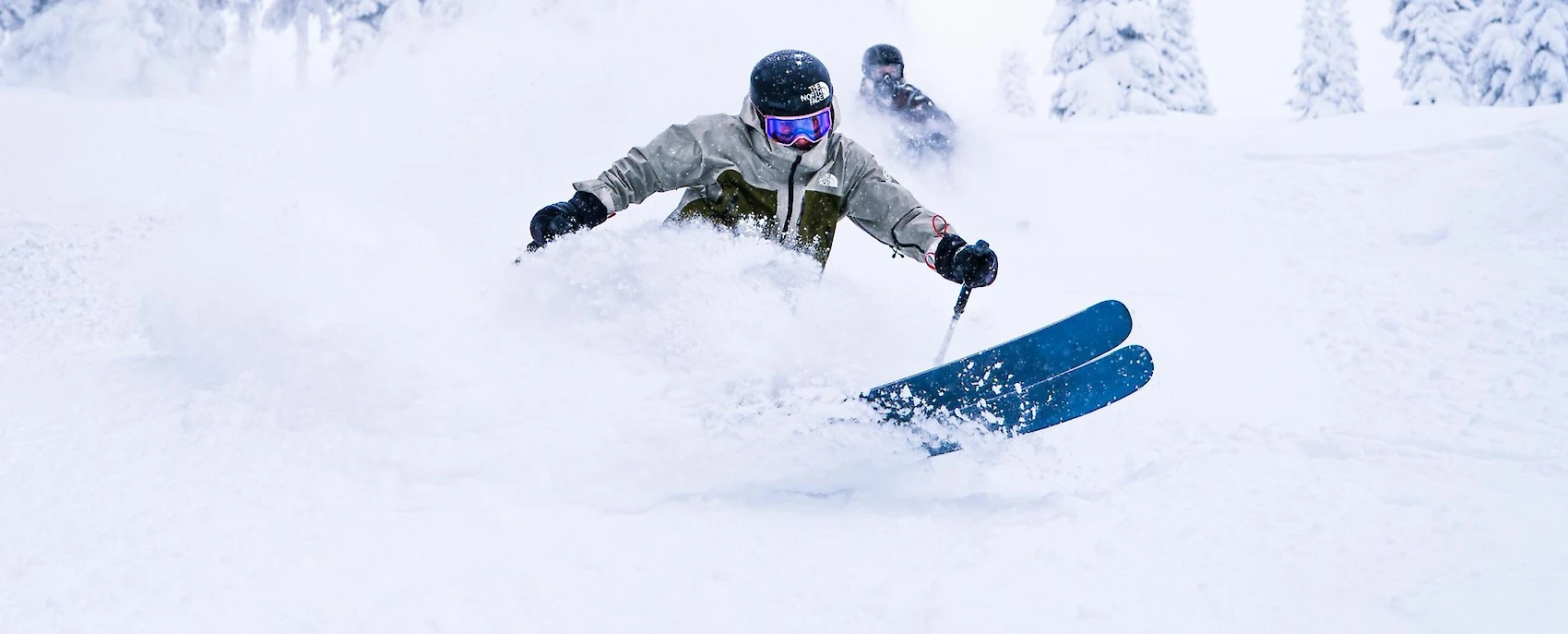 Skier dropping into deep powder through snow-covered glades on a bluebird day at Revelstoke Mountain Resort